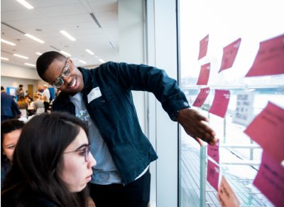 Students add sticky notes to a window during a design thinking workshop